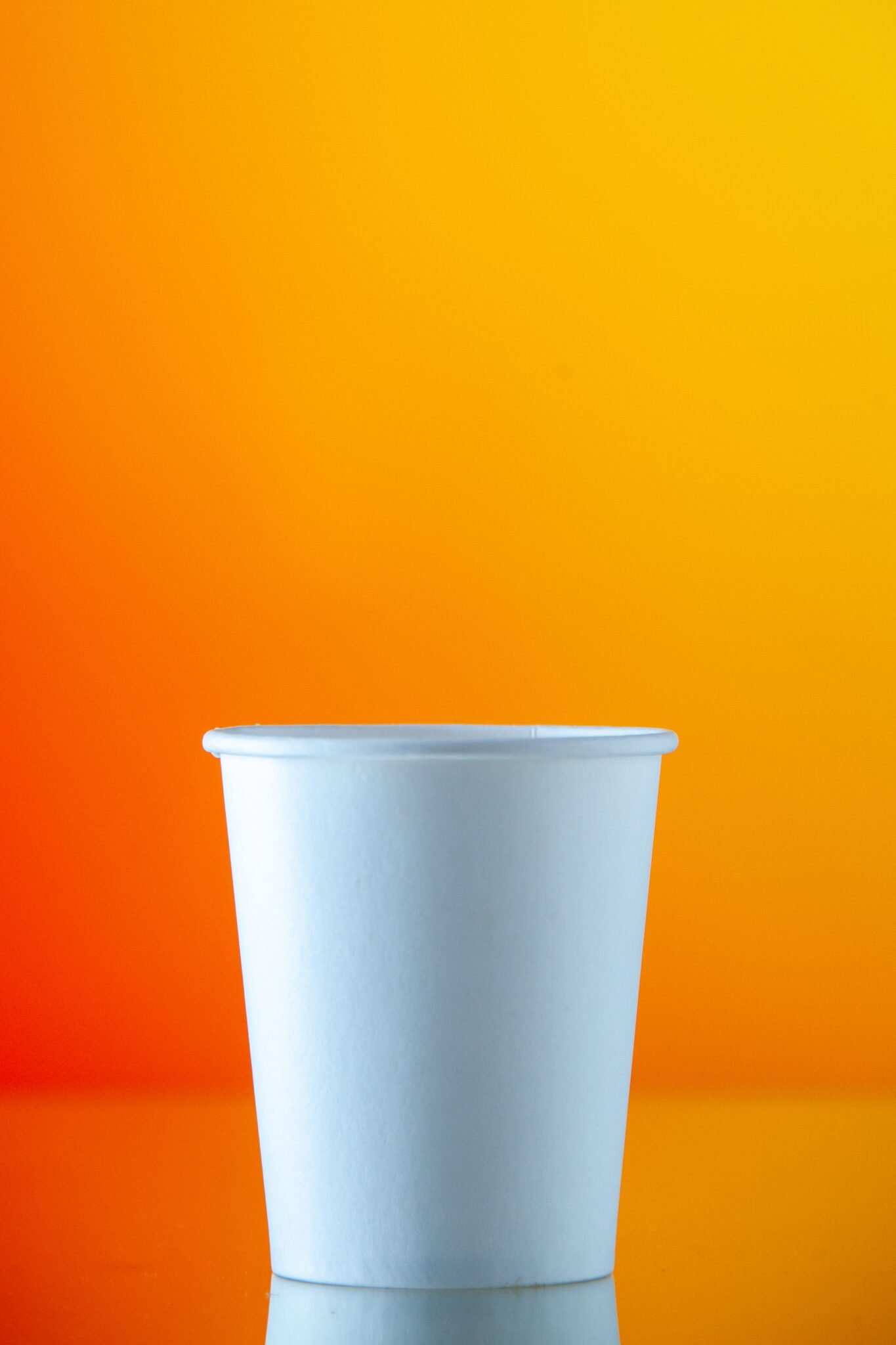 Front view of a white single wall paper cup against a vibrant orange gradient background.